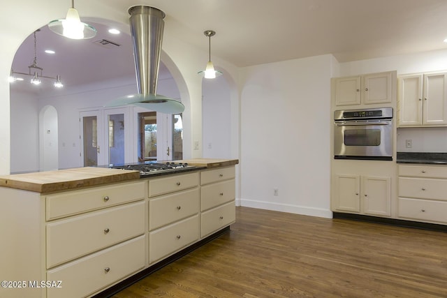 kitchen with dark wood-style floors, arched walkways, appliances with stainless steel finishes, pendant lighting, and butcher block counters