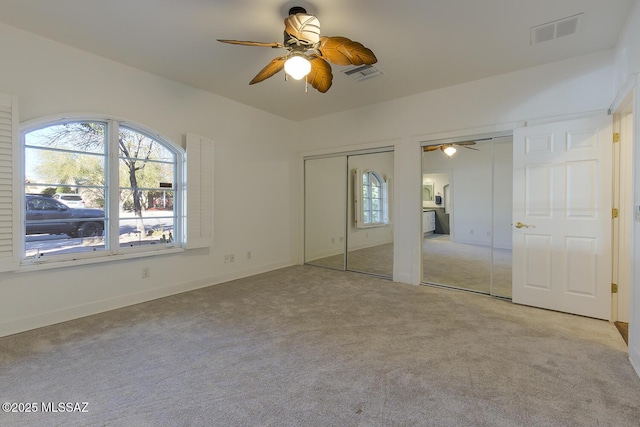 unfurnished bedroom featuring carpet, visible vents, two closets, and ceiling fan