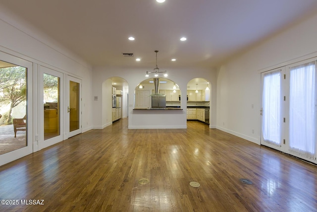 unfurnished living room featuring recessed lighting, wood finished floors, visible vents, and arched walkways