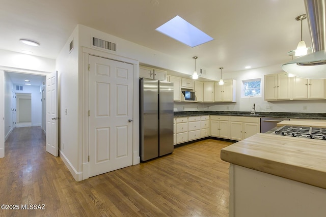 kitchen featuring visible vents, a skylight, wood finished floors, hanging light fixtures, and stainless steel appliances