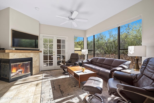 living room with a tiled fireplace, ceiling fan, and french doors