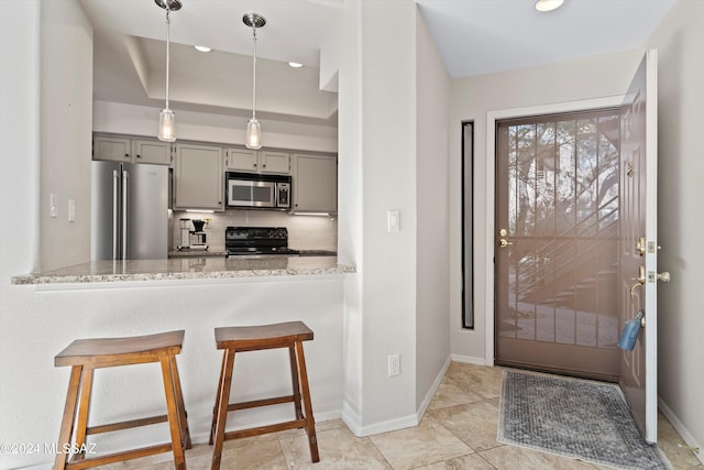 kitchen with decorative backsplash, light stone counters, gray cabinetry, stainless steel appliances, and a tray ceiling