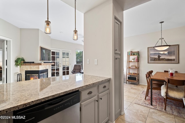 kitchen featuring pendant lighting, stainless steel dishwasher, light stone countertops, a fireplace, and light tile patterned floors