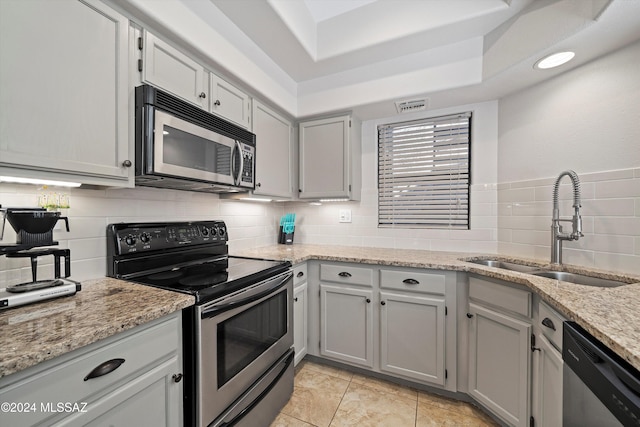 kitchen with sink, light stone countertops, appliances with stainless steel finishes, tasteful backsplash, and a tray ceiling