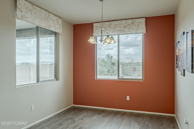 unfurnished dining area featuring baseboards, wood finished floors, a healthy amount of sunlight, and a notable chandelier