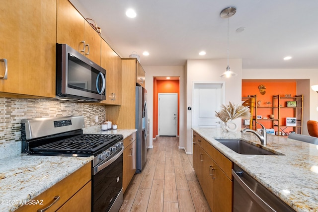 kitchen featuring tasteful backsplash, light wood-style flooring, appliances with stainless steel finishes, hanging light fixtures, and a sink