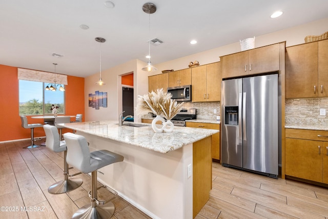 kitchen featuring hanging light fixtures, a kitchen island with sink, stainless steel appliances, wood finish floors, and a sink