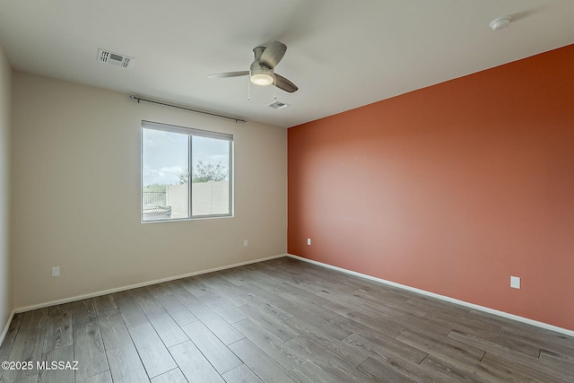 empty room featuring wood finished floors, ceiling fan, and visible vents
