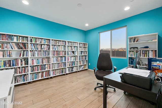 office area with light wood finished floors, recessed lighting, and bookshelves