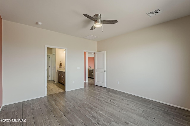 unfurnished bedroom featuring wood finished floors, ensuite bathroom, baseboards, visible vents, and ceiling fan