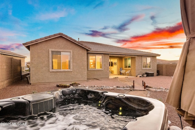 back of house at dusk featuring a tile roof, stucco siding, a hot tub, a patio area, and a fenced backyard