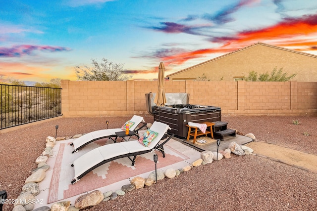 patio terrace at dusk with a fenced backyard and a hot tub