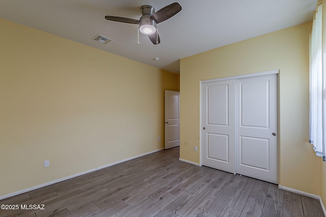 unfurnished bedroom with a closet, visible vents, wood finished floors, and baseboards