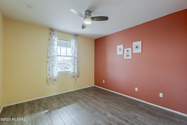 spare room featuring baseboards, wood finished floors, and ceiling fan