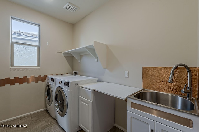 clothes washing area featuring visible vents, wood finish floors, a sink, cabinet space, and washer and clothes dryer