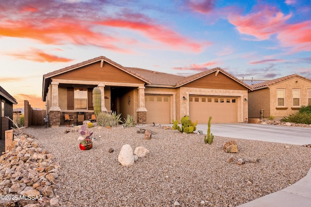 view of front of property with an attached garage, a tile roof, driveway, stone siding, and stucco siding