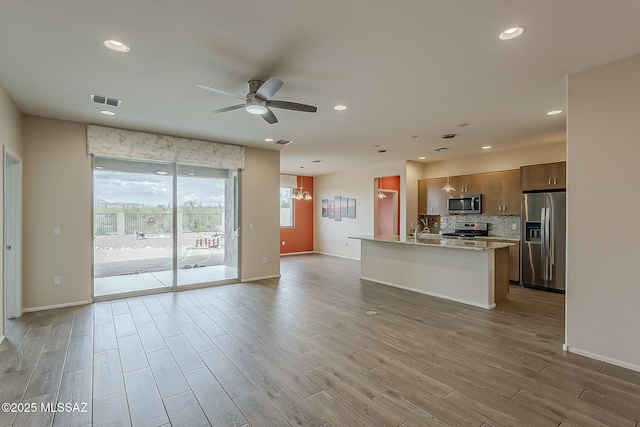 kitchen featuring open floor plan, ceiling fan, stainless steel appliances, visible vents, and decorative backsplash