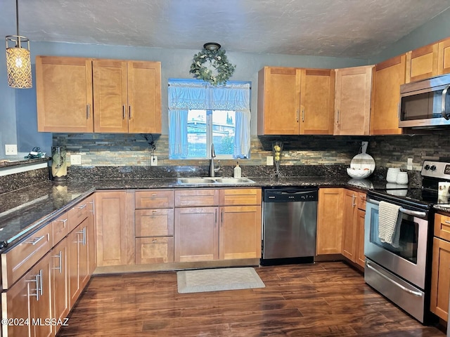 kitchen with appliances with stainless steel finishes, sink, decorative light fixtures, dark stone countertops, and dark hardwood / wood-style floors