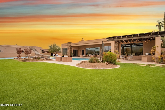 back house at dusk with a lawn, a patio area, and an outdoor hangout area