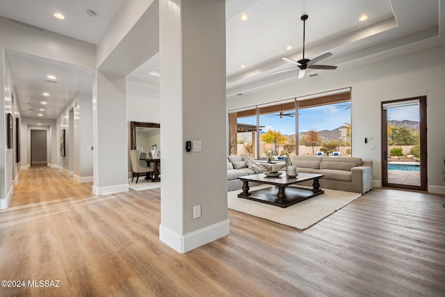 living room with ceiling fan, light wood-type flooring, and a towering ceiling