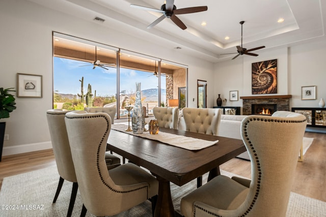 dining room featuring a stone fireplace, light wood-type flooring, and a tray ceiling