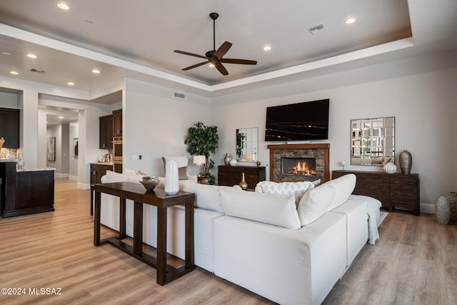 living room featuring a tray ceiling, ceiling fan, a fireplace, and light hardwood / wood-style floors