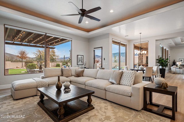 living room with a mountain view, light wood-type flooring, ceiling fan with notable chandelier, and a wealth of natural light