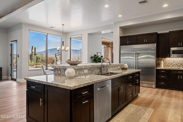 kitchen with a mountain view, sink, built in appliances, an island with sink, and light hardwood / wood-style floors