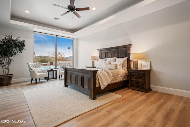 bedroom featuring ceiling fan, light wood-type flooring, and a tray ceiling