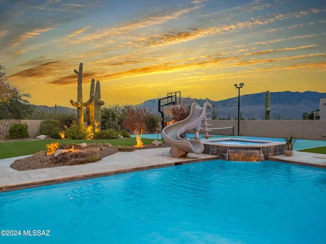 pool at dusk with an in ground hot tub, a mountain view, and a water slide