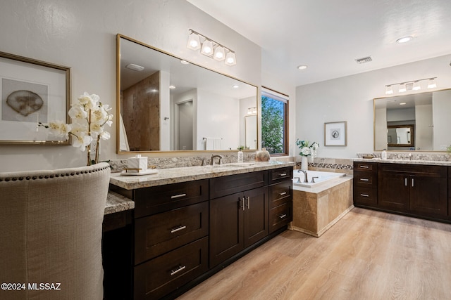 bathroom with hardwood / wood-style floors, vanity, and a relaxing tiled tub