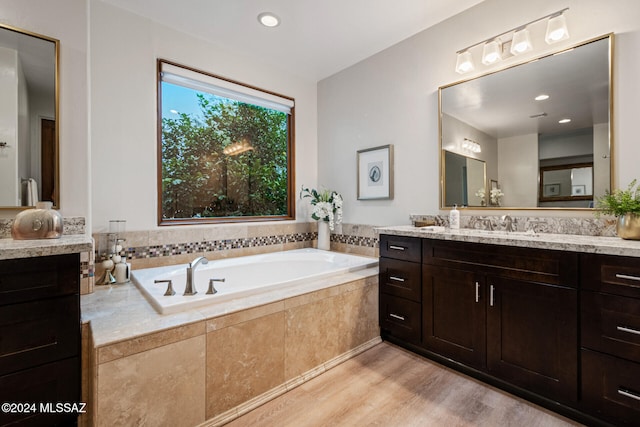 bathroom with hardwood / wood-style flooring, vanity, and a relaxing tiled tub