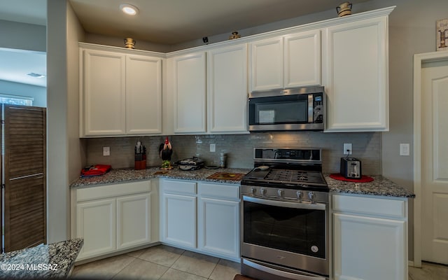 kitchen with white cabinets, dark stone countertops, light tile patterned floors, and appliances with stainless steel finishes