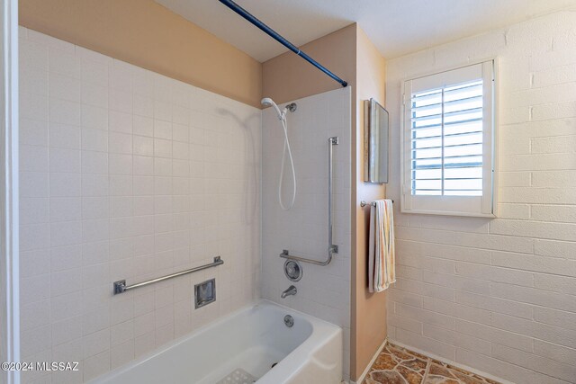 bathroom with tiled shower / bath and brick wall