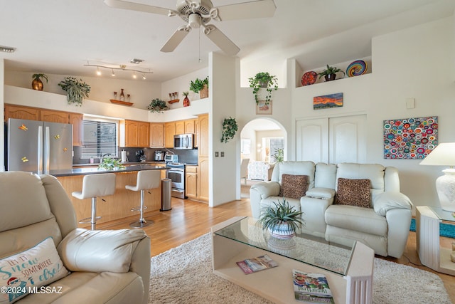 living room with ceiling fan, light hardwood / wood-style flooring, and a towering ceiling