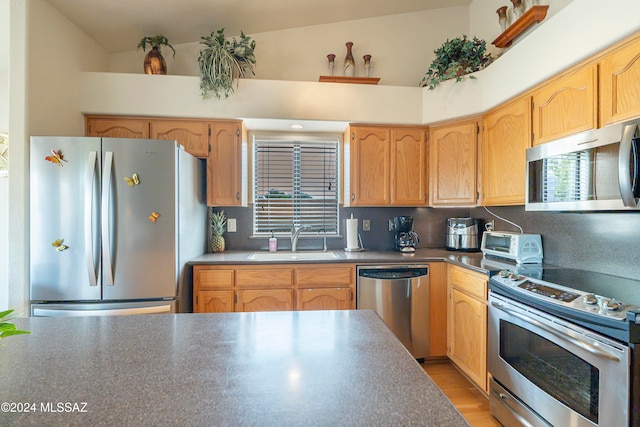 kitchen with lofted ceiling, sink, light hardwood / wood-style flooring, decorative backsplash, and appliances with stainless steel finishes