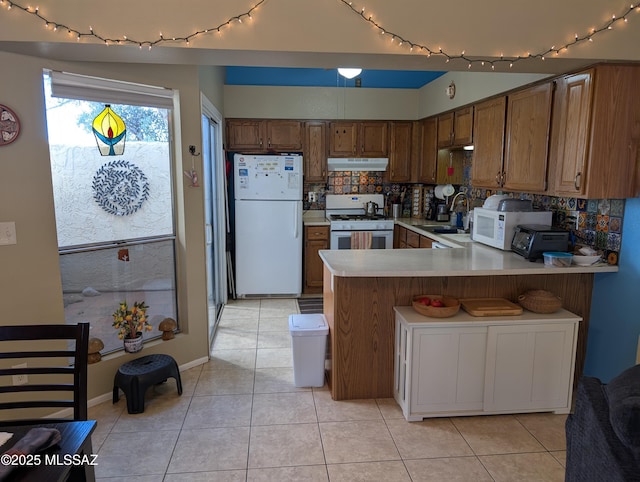 kitchen with kitchen peninsula, decorative backsplash, white appliances, sink, and light tile patterned flooring