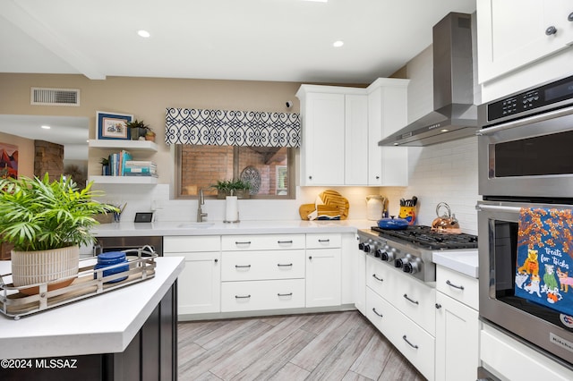 kitchen with visible vents, a sink, backsplash, appliances with stainless steel finishes, and wall chimney range hood