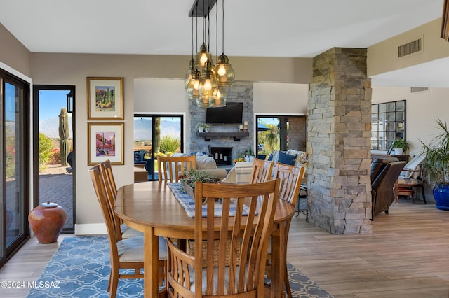 dining space featuring visible vents, light wood-type flooring, decorative columns, a fireplace, and a notable chandelier