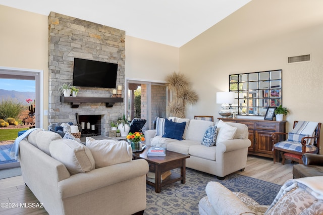 living area featuring a stone fireplace, wood finished floors, visible vents, and high vaulted ceiling