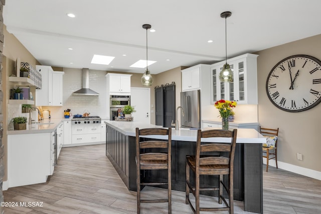 kitchen with a sink, decorative backsplash, light countertops, appliances with stainless steel finishes, and wall chimney exhaust hood