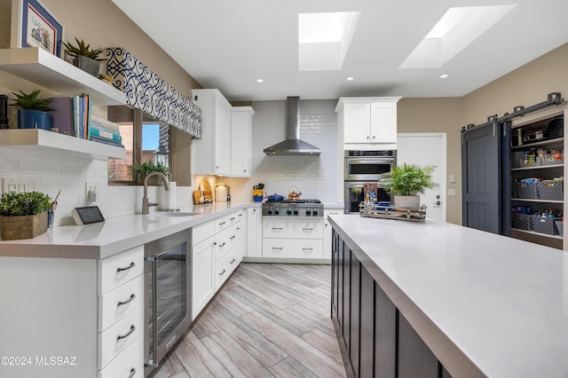 kitchen with open shelves, a sink, wine cooler, appliances with stainless steel finishes, and wall chimney range hood