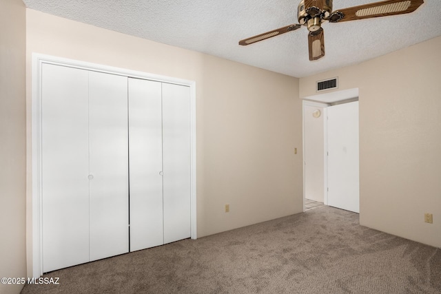unfurnished bedroom with a textured ceiling, carpet flooring, visible vents, a closet, and a ceiling fan