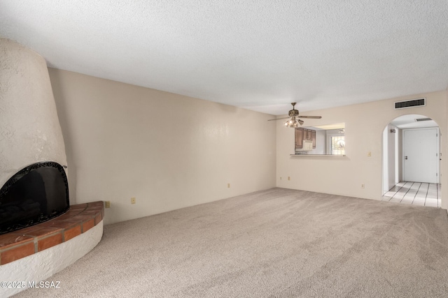 unfurnished living room featuring arched walkways, a ceiling fan, visible vents, light carpet, and a textured ceiling