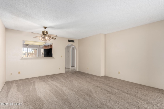 carpeted empty room with a textured ceiling, visible vents, a ceiling fan, and arched walkways