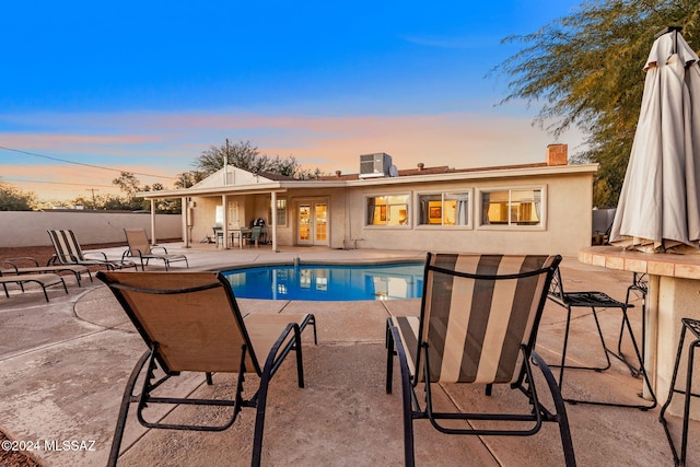 pool at dusk featuring french doors and a patio