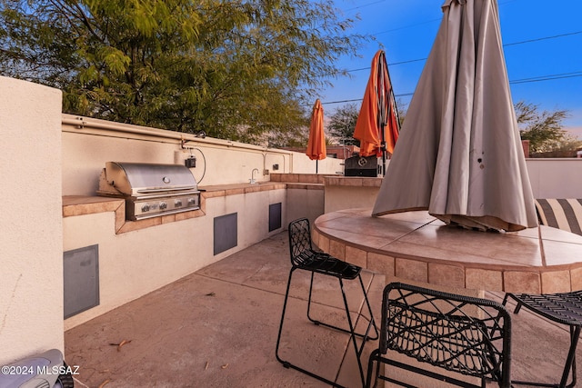 patio terrace at dusk with an outdoor wet bar, grilling area, and exterior kitchen
