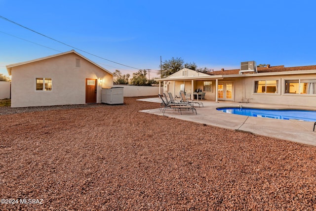 back house at dusk with a fenced in pool, cooling unit, and a patio area