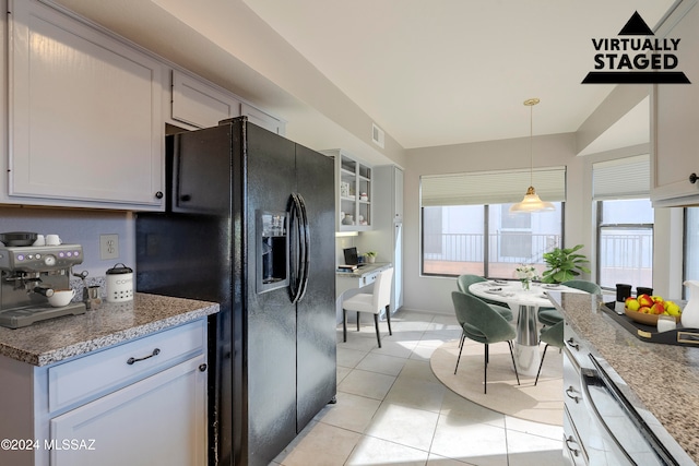 kitchen featuring pendant lighting, white cabinets, black fridge, light tile patterned floors, and light stone counters