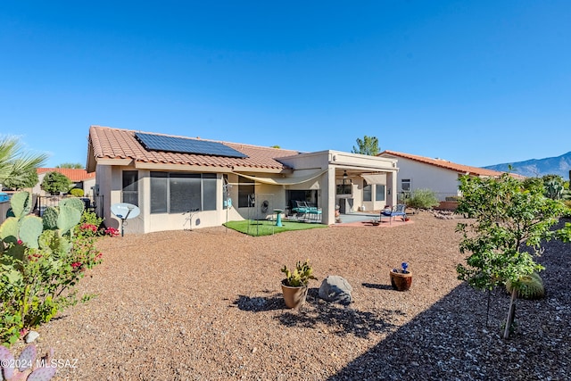 back of house with a sunroom, solar panels, a mountain view, ceiling fan, and a patio area